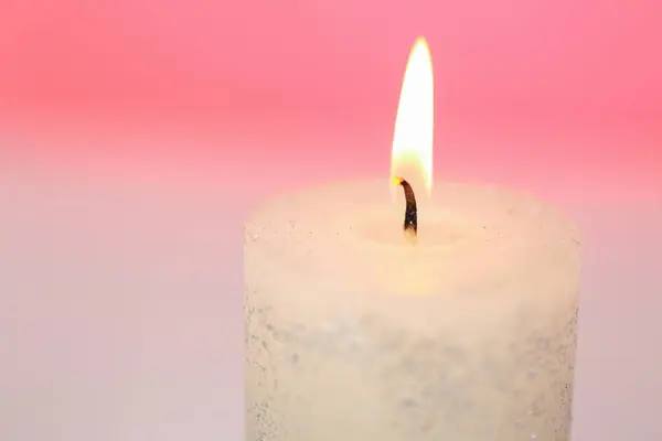Candle flame.White candle close-up on a pink background.Beautiful background with a candle in pastel colors.Burning candle close-up.