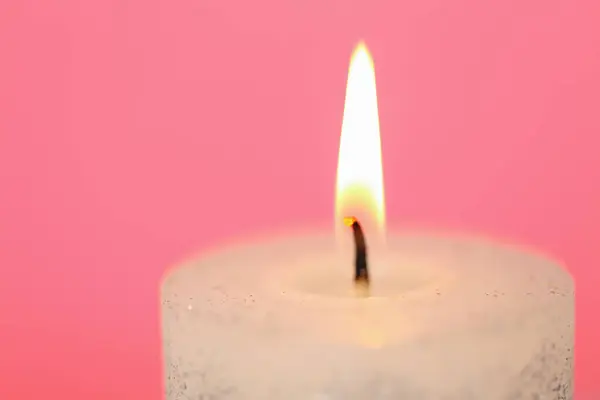 Burning candle close-up.Candle flame.White candle close-up on a pink background.Beautiful background with a candle in pastel colors
