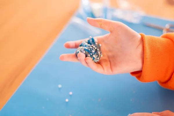 Blue slime in childrens hands on a blue silicone mat on a wooden table. View from above.Fine motor skills development.Soft plasticine in hands.Childrens creativity and development. Childrens games and