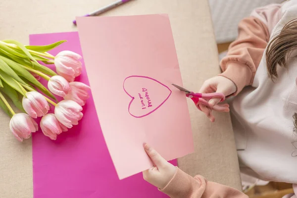 moms day concept. DIY mom card.Child cuts a heart out of paper at the table. View from above.child makes a card for his mother.Flowers and cards for mom.