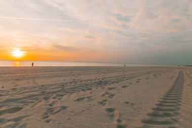 İnsanlar gün batımında deniz kıyısında yürürler. Almanya 'da kötü bir tatil. Fer Adası. Frizya Adaları Sahili .