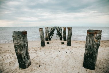 Bulutlu bir günde denizde ahşap iskele. Wadden Deniz Kıyısı ve ahşap sütunlar. Gelgit zamanı..