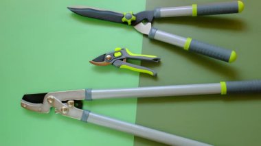 Bitki Büzme Aracı. Secateurs, loppers ve çim biçme makineleri yeşil arka planda. Bahçe ekipmanları ve aletleri. Bitkileri budamak ve budamak için aletler. 4k görüntü