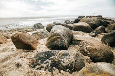 Stone boulders on the beach at low tide.Wadden Sea Coast.Stone groyne close-up on cloudy sky background.. Marine photo wallpaper.Nature of the North Sea coast.  clipart