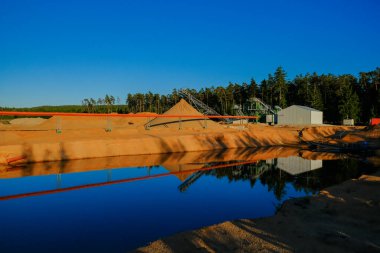 Kum madenciliği. Kum madenciliği için endüstriyel ekipman. Kum çıkarmak için gerekli ekipmanlar bir göletin kıyısında, bir çam ormanıyla çevrilidir. Kum ocağı.