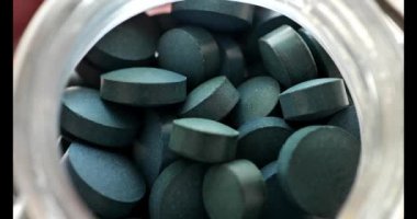 Camdan bir kavanozda yaklaş. Yeşil kuru spirulina tabletleri. Tabletlerdeki algler. Süper yiyecek. Sağlıklı bir yaşam tarzı için gıda takviyesi. Doğal iyot kaynağı. 4k görüntü