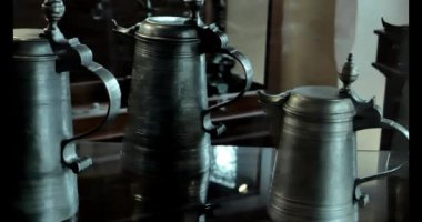 Kapaklı metal kupalar. Antika teneke aletler, teneke çatal bıçak takımı ve cam bir vitrindeki metal tabaklar. Klasik sofra takımı. 4k görüntü