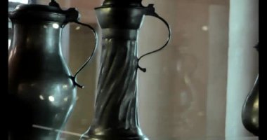 Teneke sürahiler. Çanak çömlek ve tenekeden yapılmış çatal bıçak takımı. Cam bir vitrinde metal antika tabaklar. Klasik sofra takımı. 4k görüntü