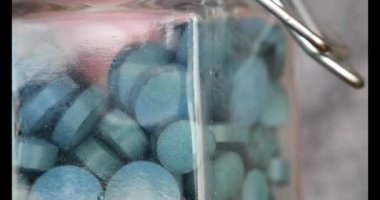 Zeytinyağı tabletleri. Parmaklar cam bir kavanozdan spirulina kapsülleri alır. Zülkül insan emilimi. Yeşil kuru spirulina tabletleri. Sağlıklı bir yaşam için gıda takviyeleri. Vitaminler ve beslenme takviyeleri.. 