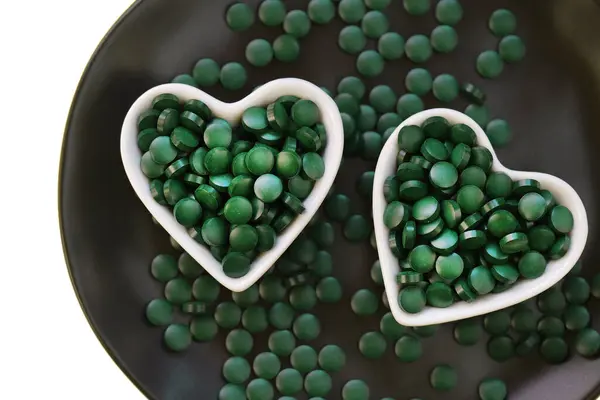 Stock image  spirulina tablets in white heartshaped cups on a black tray isolated on a white background.Natural source of iodine. Super food . 