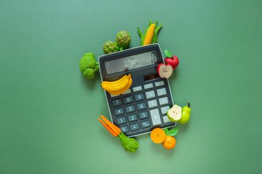 Yiyecek maliyeti. Yükselen gıda fiyatları. Yeşil arka planda hesap makinesi ve sebze deco. Sebze ve meyve fiyatlarında artış. Yemek sepeti maliyeti..
