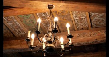 Ahşap tavanın altında asılı antik bir avize. Parlayan avize geleneksel bir ayarı aydınlatıyor. Klasik Aydınlatma Tasarımı. Antik Işıklandırma Güzelliği. 4k görüntü