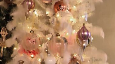 Noel baloları ve pastel renkli oyuncaklar. Kar taneleri, tüyler ve kumaş çiçekleriyle beyaz ve pembe renklerde Noel arkaplanı. Parlayan çelenkler ve Noel dekoru. 4k görüntü