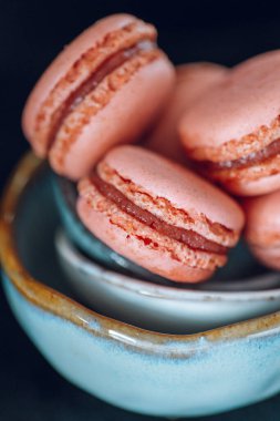  Siyah arka planda gri bir seramik fincana saçılmış makaronlar. Yumuşak anahtar. Şekerler ve tatlılar. Fransız hamur işleri hazır. Makarna kek seti. 