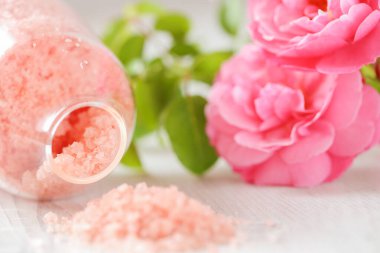 Gül özlü gül tuzu. Cam kavanozlarda spa tuzu ve eski püskü beyaz arka planda pembe güller. Aromaterapi ve kozmetik ürünleri. Gül çiçekleri ve pembe kozmetik tuzları. Organik kozmetik tuz. 