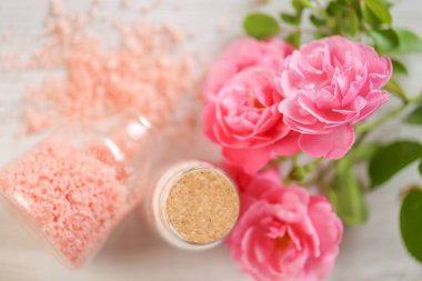 aromatik pembe tuz. Cam kavanozlarda spa banyosu tuzları ve pejmürde beyaz arka planda pembe güller. Gül özü ve güzel kokulu gül tuzu. Aromaterapi ve kozmetik. Organik kozmetik tuz.