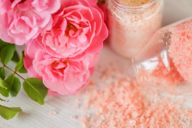 aromatik pembe tuz. Cam kavanozlarda banyo tuzu ve pejmürde beyaz arka planda pembe güller. Gül özü ve güzel kokulu gül tuzu. Aromaterapi ve kozmetik. Organik kozmetik tuz.