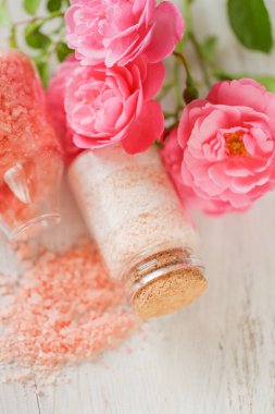 Gül kokulu pembe tuz. Gül özlü kozmetik ürünü. Cam kavanozlarda spa banyosu tuzu ve eski püskü beyaz arka planda pembe güller. Romaterapi ve kozmetik.