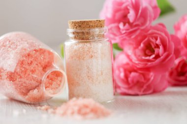 Gül özlü gül tuzu. Cam kavanozlarda spa banyosu tuzu ve eski püskü beyaz arka planda pembe güller. Aromaterapi ve kozmetik ürünleri. Gül çiçekleri ve pembe kozmetik tuzları. Organik kozmetik tuz. 