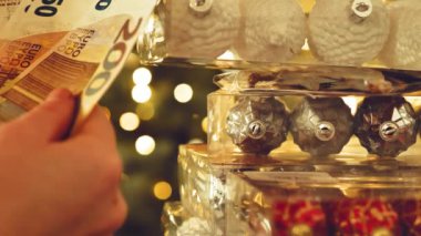 Noel süslemeleri ve hediyeler almak. Avro banknotlarını saymak ve Bokeh çelenklerinin parladığı kutularda Noel süsleri görmek. Noel tatili masrafları. 4K görüntü.