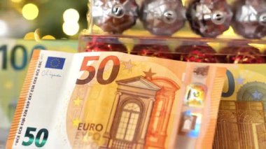 Noel harcamaları ve harcamaları. Avro banknotları ve Noel oyuncakları, Noel ağacı arka planında parlayan çelenklerle dolu kutularda. Tatil Masrafları. 4k görüntü