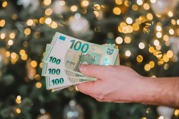 Noel harcamaları. Kış tatillerinde ödenecek paralar. Erkekler, çelenklerle süslenmiş bir Noel ağacının şenlikli zeminine karşı avroluk banknotları sayıyor. Noel ve Yeni Yıl alışverişi ve