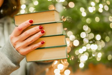 Noel kitabı. Elinde yeşil kapaklı kitaplarla Noel ağacı arka planında. Kış tatillerinde kitap okuyor..