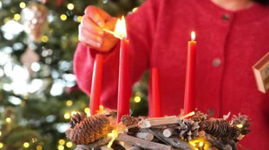 Kırmızı mumlu Advent çelengi. Dördüncü Advent. Noel 'den dört hafta önce. Kırmızı kazaklı kadın, Noel ağacının arka planında Advent çelenginin ilk mumu. Noel gelenekleri. 