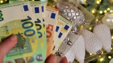 Euro banknotları ve Noel ağacı arka planında Noel oyuncakları. Noel alışverişi. Noel ağacı süslemeleri. Kış Tatili Mevsimi Nakit Harcama. 4k görüntü