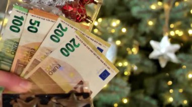 Noel ağacı süslemeleri. Euro banknotları ve Noel ağacı arkaplanındaki Noel ağacı oyuncakları. Kış Tatili Mevsimi Nakit Harcamaları. 4k görüntü