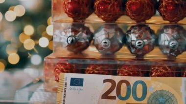 Noel harcamaları. Euro banknotları ve altın bokeh çelenkleri üzerine parlak Noel ağacı süslemeleri. Kış bayramı sembolü. 4k görüntü