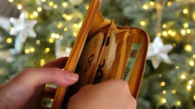 Noel ağacı süslemeleri. Eller Noel ağacının arka planındaki cüzdandan para alıyor. Kış Tatili Mevsimi Nakit Harcamaları. 4k görüntü