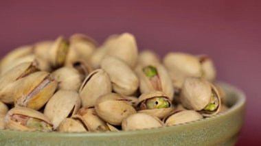 Bordo bir arka planda yeşil bir fincanda fıstıklar. Dönüşümlü. Sağlıklı, bitkisel beslenme. Vejetaryen ve vejetaryen yemekleri. 4k görüntü