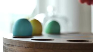Ahşap bir stantta paskalya yumurtaları. Geleneksel Paskalya masası. El, boyalı yumurtaları parlak bir odadaki masanın üstüne koyar. 4k görüntü