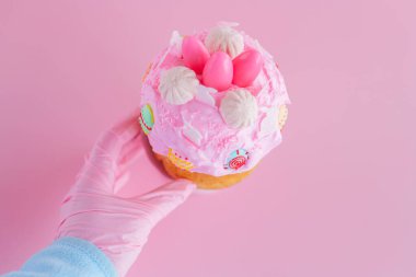 Pembe arka planda pembe eldivenli paskalya pastası. El ele tutuşan pembe şekerli pasta. Paskalya için moda tasarım. Paskalya yemeği. Şenlikli Pişirme