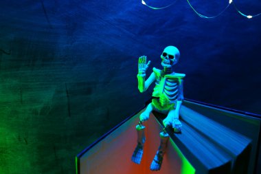 Cadılar Bayramı Hikayeleri. İskelet Oyuncak Işıklarla Oturuyor. Kitap, iskelet ve parıldayan çelenk.. 