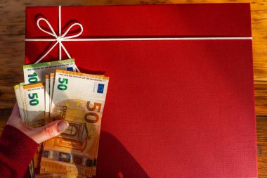 Kırmızı Paketli Hediyenin Yanında Nakit Hediye. Hediye almanın bedeli. Avro faturalı kırmızı hediye kutusu. Bayram Hediyelik Eşyalar. Hediye çeki konsepti.. 