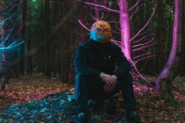 Karanlık Orman 'da oturan Korkunç Balkabağı Kafa. Balkabağı canavarı sonbahar ormanında oturuyor Ürkütücü mavi ve mor bir ışıkta