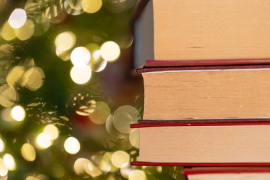  Kış kitapları. Kırmızı kapaklı kitaplar Noel ağacının arka planına istiflenir. Bokeh özgeçmişi olan bir yığın kitap. Kış atmosferik tatil kitapları.