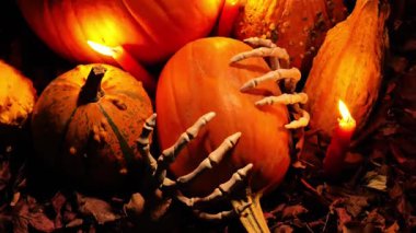 Cadılar Bayramı atmosferi. Balkabağı sonbahar yapraklarında mum ışığında iskelet ellerde. Balkabağı seti, kemik eller ve karanlıkta kırmızı mumlar. 4k görüntü