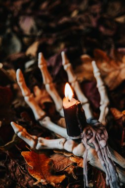 Ürkütücü Cadılar Bayramı Mumları. Sonbahar Yaprakları 'nda İskelet El Tutma Mumları. Cadılar Bayramı mumları. Sonbahar Yaprakları ile İskelet El' de Yanan Mum..