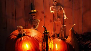 İskelet bayramı arka planı. Büyücü şapkasındaki kemik heykelciği. Kırsal bir zeminde yanan mumlar ve balkabakları. 4k görüntü