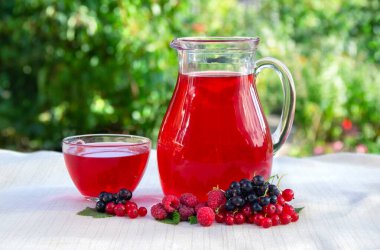 Sürahide kırmızı meyveli içecek, cam bardak, olgun kırmızı ahududu, kuşüzümü, yeşil doğa arkaplan üzerinde kırmızı frenk üzümü ve metin için yer var.