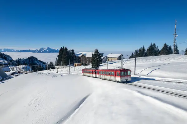 Kışın Rigi İstasyonu 'ndan ayrılan kırmızı bir Vitznau Rigibahn treni görülüyor. Arka plandaki Pilatus Dağı görülebilir..