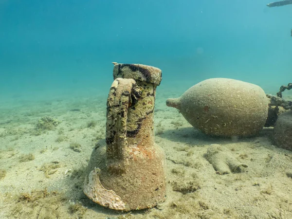 Antique amphoras on a sandy sea floor. Beautiful turquoise water in the background