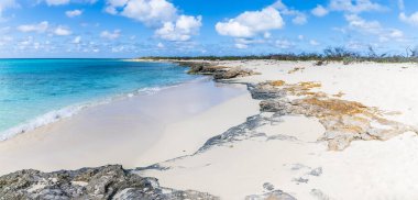 A view of a rocky shoreline and white pristine sand on the island of Grand Turk on a bright sunny morning
