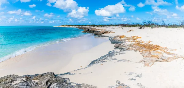 A view of a rocky shoreline and white pristine sand on the island of Grand Turk on a bright sunny morning