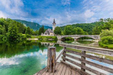 Slovenya 'nın Bohinjsko Jezero kentindeki Vaftizci Yahya Kilisesi ve köprüye doğru giden ahşap iskeleden bir manzara