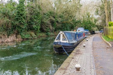 Kışın Market Harborough 'daki donmuş Grand Union kanalının yanındaki sahil yolu boyunca demirlemiş teknelerin yanından bir manzara.