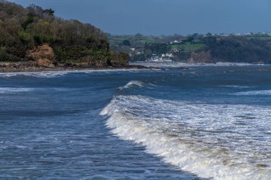 A view of surf breaking off the beach in the village of Saundersfoot, Wales on a bright spring day clipart